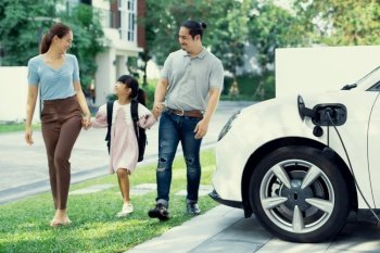 Progressive young happy family with electric vehicle and home backyard charging station. Green and clean energy from electric vehicles for healthy environment. Eco power from renewable source.. Progressive young happy family living in a home with an electric car.