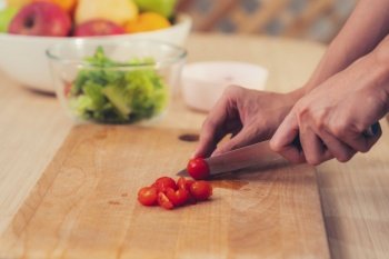 Close up hands holding a knife preparing a contented meal. Sliced tomatoes and other vegetables on the glass dish.. Close up hands holding a knife preparing a contented meal.