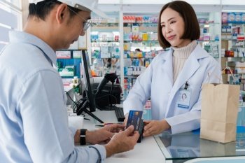 Payment by credit card with payment terminal in qualified drugstore. Modern financial payment of electric money. Caucasian customer purchase medication in pharmacy with prescription from pharmacist.. Customer purchases qualified prescription medical drugs from pharmacist.
