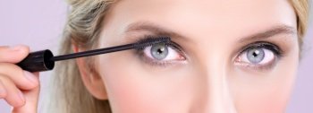 Closeup woman with blond hair putting alluring black mascara with brush in hand on long thick eyelash. Perfect fashionable cosmetic clean facial skin with beautiful eye young woman in high resolution.. Closeup beautiful woman putting alluring black mascara on long thick eyelashes.