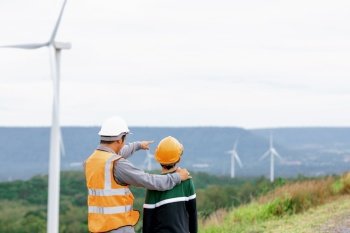 Engineer with his son on a wind farm atop a hill or mountain in the rural. Progressive ideal for the future production of renewable, sustainable energy. Energy generation from wind turbine.. Progressive engineer with his son in the wind farm atop of the mountain.
