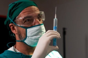 Surgeon fill syringe from medical vial for surgical procedure at sterile operation room. Doctor in full protective wear for surgery prepare anesthesia injection for his patient. Surgeon fill syringe from vial for surgical procedure at sterile operation room.
