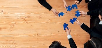 Top view businesspeople and colleagues in formal wear putting jigsaw puzzles together over meeting table with financial report papers in harmony office for team building concept.. Top view businesspeople a putting jigsaw puzzles together in harmony office.