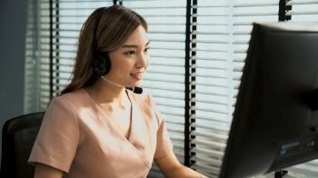 Competent female operator working on computer and while talking with clients. Concept relevant to both call centers and customer service offices.. Competent female operator working on computer and while talking with clients.