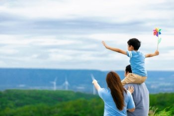 Progressive happy family enjoying their time at wind farm for green energy production concept. Wind turbine generators provide clean renewable energy for eco-friendly purposes.. Progressive happy family enjoy their time at wind farm for green energy concept.