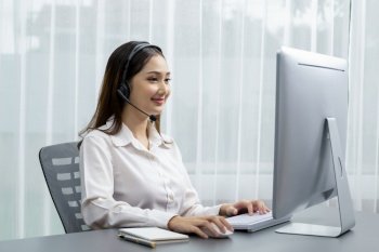 Asian call center with headset and microphone working on her laptop. Female operator provide exceptional customer service. Supportive call center agent helping customer on inquiry. Enthusiastic. Enthusiastic asian call center with headset and microphone working on her laptop