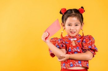 Chinese New Year. Happy Asian Chinese little girl smile wear red cheongsam qipao hold angpao red packet monetary gift, Portrait child in traditional dress, studio short isolated on yellow background
