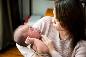 Parent woman cuddling baby tenderness, Asian mom holding her crying little baby at home, Mother comforts little son or daughter newborn, cry after birth