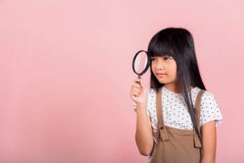 Asian little kid 10 years old funny looking through magnifying glass at studio shot isolated on pink background, Happy child girl lifestyle smiling exploring holding magnifier searching