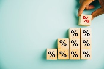 Concept of interest rate and financial rates. Hand placing a wooden cube block on top, symbolizing an upward direction and an increase, with a prominent percentage symbol.