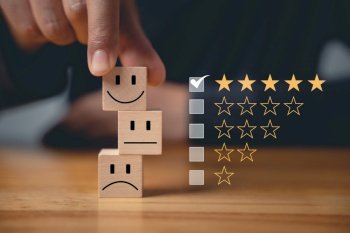 5-star satisfaction is guaranteed with a wooden block cube’s smiley face selected by a businessman’s hand. Satisfaction survey and feedback concept for the best customer experience.