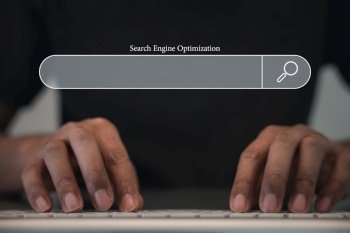 Man’s finger indicating the search icon on a dark background, while using a computer keyboard for searching and browsing internet data. The networking and searching concept is highlighted