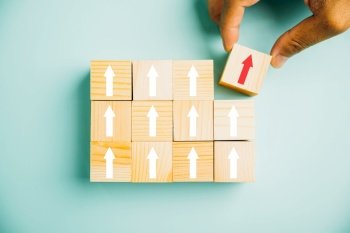Male hands carefully arranging wooden blocks as steps, symbolizing the path to business growth. The upward arrow signifies the rise in performance, potential, and success. Copy space for customization