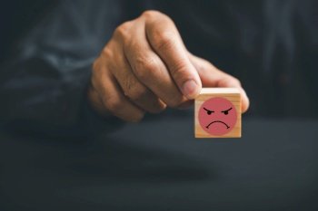Customer dissatisfaction concept. Unhappy customer hand with a sadness emotion face on a wooden block. Bad service, low rating, and negative feedback affecting business reputation in online marketing.