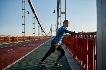 Man runner doing stretching workout before running marathon in urban bridge city background. Man runner doing stretching workout before running marathon