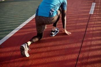 Portrait of adult speed runner in starting position ready for running on sports track. Closeup view. Adult speed runner in starting position ready for running on sports track
