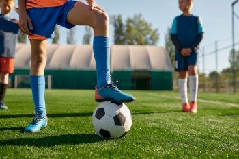 Young soccer player holding boots on ball cropped shot. Kids team practicing soccer on grass venue. Young soccer player holding boots on ball cropped shot