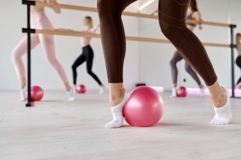 Low section view at row of women stretching feet using fitness ball. Aerobics training, pilates workout or yoga exercising at female fit club. Low section view at row of women stretching feet using fitness ball