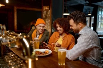 Excited diverse friends having fun watching football game online video on smartphone Three millennial multiracial young people rest in sports bar. Friends watching football game online video on smartphone rest in sports bar