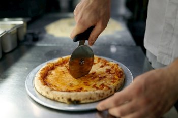 Chef cutting freshly baked pizza with round knife on wooden board. Man slicing tasty italian pastry closeup. Chef cutting freshly baked pizza with round knife on wooden board