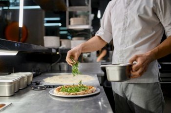Chef sprinkling fresh greenery over traditionally made pizza. Italian fast food restaurant. Chef sprinkling fresh greenery over traditionally made pizza