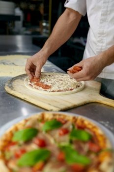 Above view on chef hand adding cheese to pizza base with sauce. Man pizzaiolo working on professional kitchen. Above view on chef hand preparing pizza base on professional kitchen