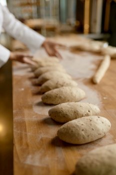 Baker working in bakery, forming baguettes from raw dough. Bakery shop and manufactory concept. Baker working in bakery, forming baguettes from raw dough