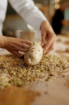 Baker shaping bread bagels, dipping dough with seeds and oatmeal flakes. Bakery shop. Baker shaping bread bagels with seeds