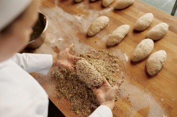 Baker shaping bread bagels, dipping dough with seeds and oatmeal flakes. Bakery house concept. Baker shaping bread bagels with seeds
