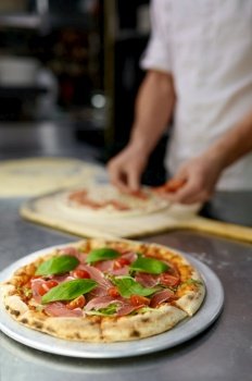 Pizza baking process closeup. Cooking Italian fast food concept. Chef hands preparing takeaway meal on blurred kitchen background. Pizza baking process closeup on freshly cooked Italian pastry