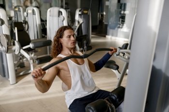 Motivated young athletic man pumping muscles having workout on gym exercising machine lifting different weights. Motivated young athletic man having workout on gym exercising machine