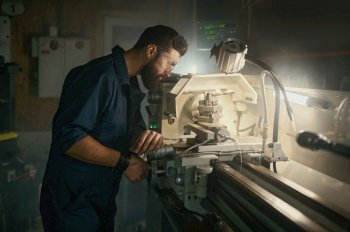 Serviceman working on turning lathe to adjust spare parts. Repair work in motorcycle workshop concept. Serviceman working on turning lathe to adjust spare parts, repair work