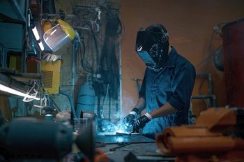 Professional repairman wearing protective helmet and overalls working with welding at motorcycle workshop. Repairman wearing protective helmet working with welding at motorcycle workshop