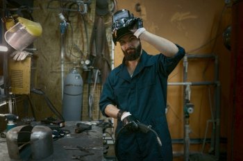 Portrait of handsome young repairman taking off protective helmet looking at camera with smile. Repair service man after hard work with welder. Portrait of repairman taking off protective helmet after hard work with welder