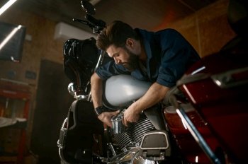 Male mechanic working in garage and repairing custom motorcycle. Creative authentic workshop concept. Male mechanic working in garage and repairing custom motorcycle