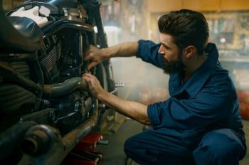 Young mechanic wearing coveralls using professional tools working on motorcycle in garage repair service. Young mechanic working on motorcycle in garage repair service