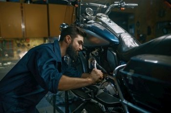 Man technician repairing motorcycle using wrench while working at repair workshop. Professional maintenance of modern and vintage motorbike concept. Man repairing motorcycle using wrench while working at repair workshop