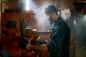 Repairman in protective glasses working on milling machine in smoky space of motorcycle workshop. Repairman working on milling machine in smoky space of workshop