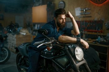 Portrait of brutal unshaven man mechanic sitting on repaired motorcycle over workshop background. Portrait of brutal man mechanic sitting on repaired motorcycle