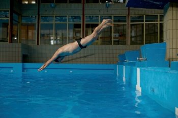 Senior man jumping in swimming pool while training indoors. Sport, hobby and active lifestyle on retirement. Senior man jumping in swimming pool while training indoors