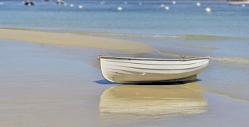 white boat placed on the sand near the blue sea with reflection on the wet sand 
