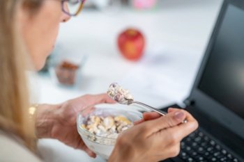 The perfect balance of work and wellness as a woman embraces healthy eating at her workplace. With a bowl of nutritious muesli and yogurt in her hand, optimizing her productivity. Woman Enjoys Muesli & Yogurt on Workplace