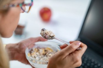 The perfect balance of work and wellness as a woman embraces healthy eating at her workplace. With a bowl of nutritious muesli and yogurt in her hand, optimizing her productivity. Woman Enjoys Muesli & Yogurt on Workplace