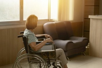 Patient sitting alone on wheelchair looking out at hospital or home care window with hope.