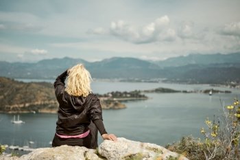 Tourist woman, sit on rocks in spring mountains over bay in Aegean sea, travel alone, hiking and adventure, healthy lifestyle outdoors, mediterranean sea nature