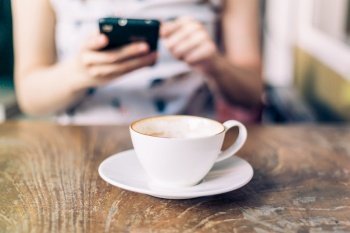 close up coffee cup with woman playing smartphone, vintage tone.
