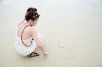 young asian women sitting on beach and drawing heart picture on sand