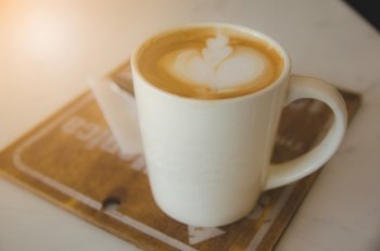 white coffee cup on wood plate on white table with leaf image foam