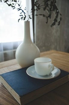white coffee cup on blue book with white vase on table