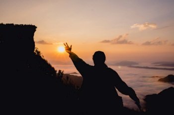 silhouette of woman standing on hill is hand up in the air